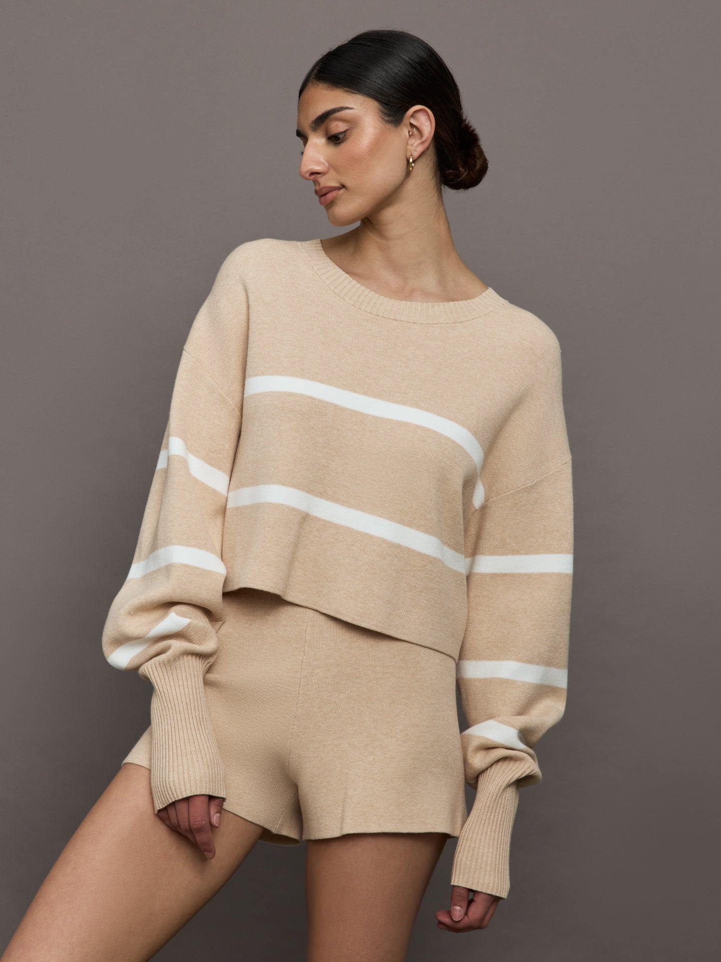 Model wears a boat neck oversized cropped khaki sweater with white horizontal stripes. 