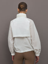 Model is wearing a white windbreaker with drawstrings at the bottom of the jacket and twin chested pockets and a detachable hood. 