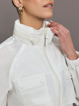 Model is wearing a white windbreaker with drawstrings at the bottom of the jacket and twin chested pockets and a detachable hood. 
