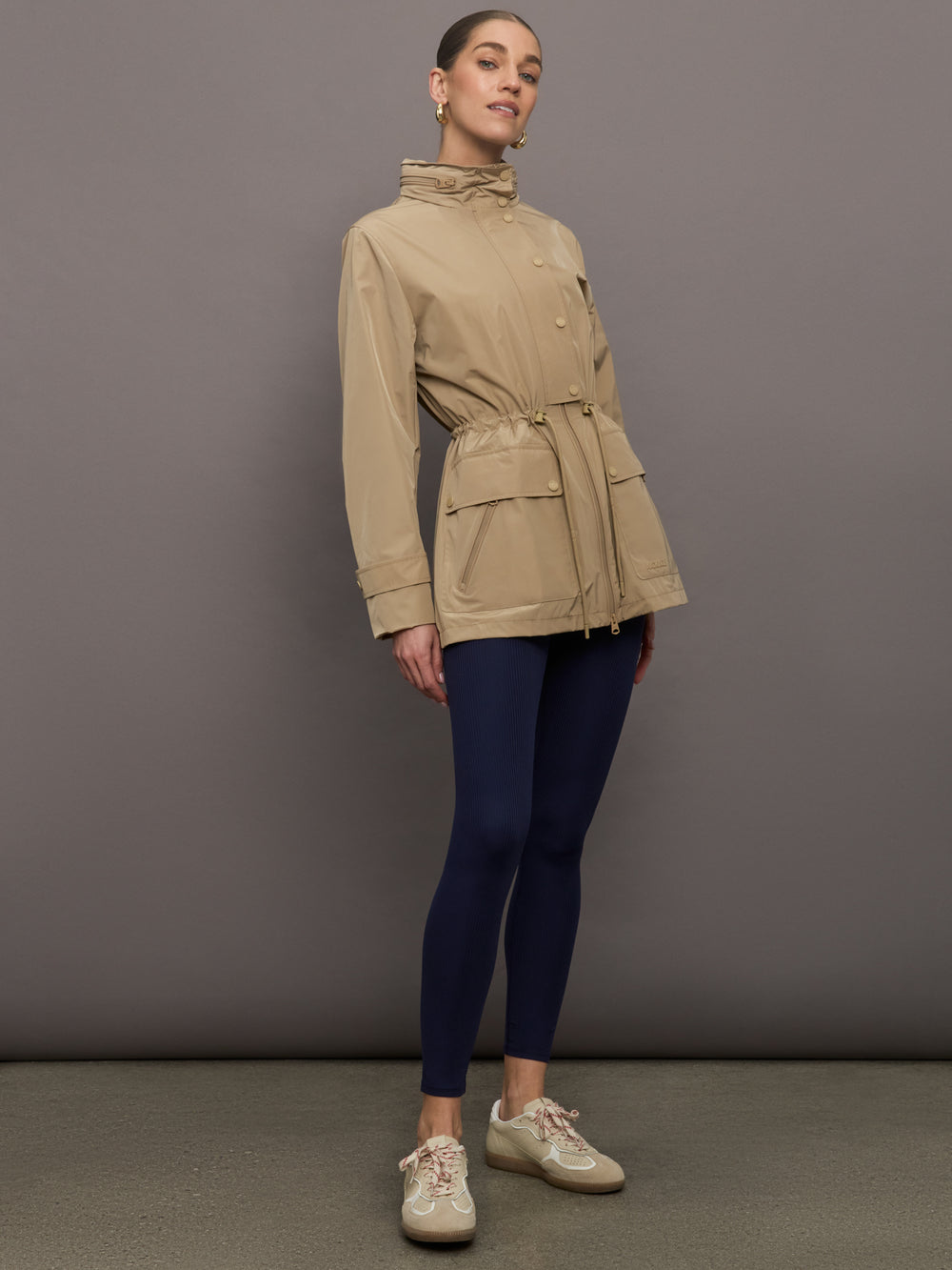 Model is wearing a tan colored rain jacket with a cinched waist.