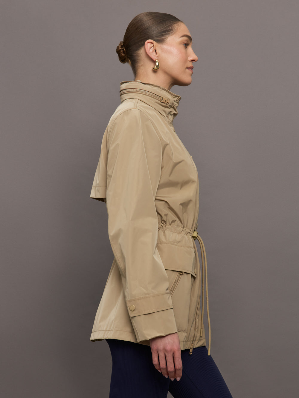 Model is wearing a tan colored rain jacket with a cinched waist.