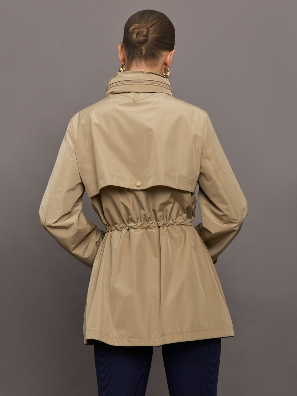 Model is wearing a tan colored rain jacket with a cinched waist.