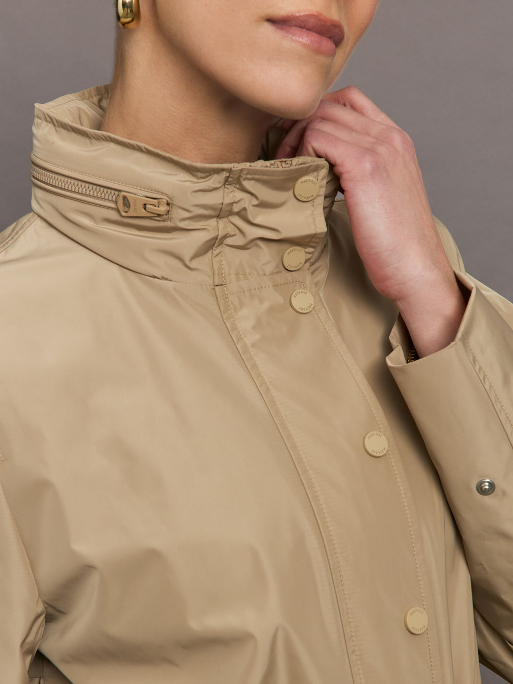 Model is wearing a tan colored rain jacket with a cinched waist.