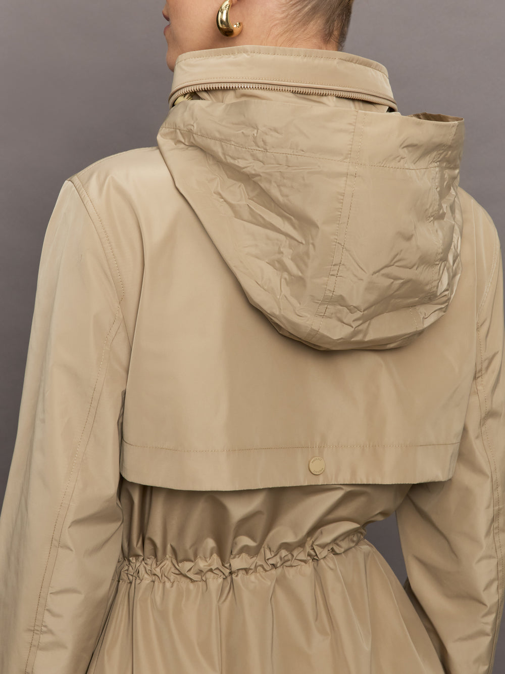 Model is wearing a tan colored rain jacket with a cinched waist.