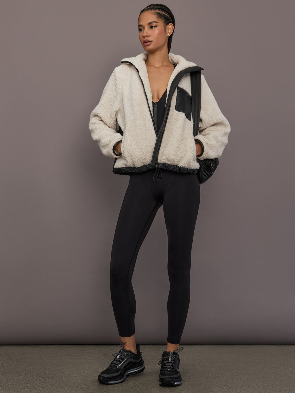 Model is wearing the Odyssey Jumpsuit in black styled with a sherpa jacket, full body view.