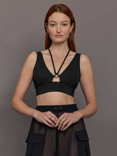 Model wears black Odyssey Longline Bra with a sleek, supportive design, featuring wide straps and a low V-neck cut.