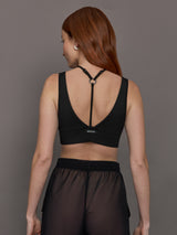 Model wears black Odyssey Longline Bra with a sleek, supportive design, featuring wide straps and a low V-neck cut.