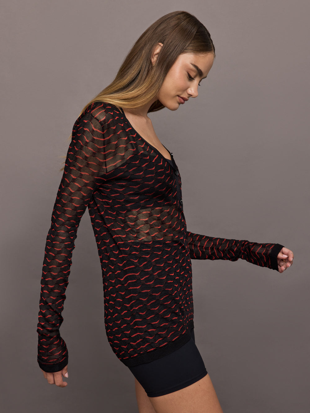 Woman wearing a black and red patterned long-sleeve top against a gray background