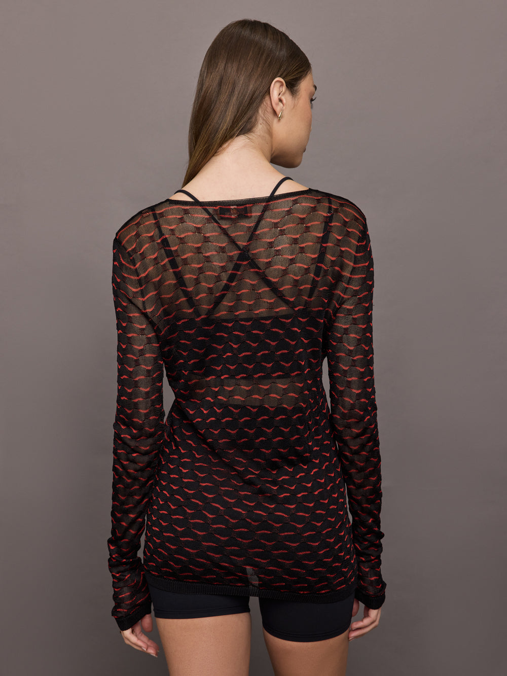 Woman wearing a black and red patterned long-sleeve top against a gray background