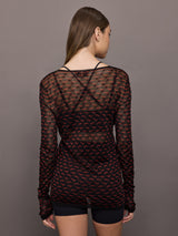 Woman wearing a black and red patterned long-sleeve top against a gray background