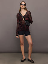Woman wearing a black and red patterned long-sleeve top against a gray background