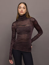 Model wears a striped sheer long sleeve turtleneck with brown and purple tones. 