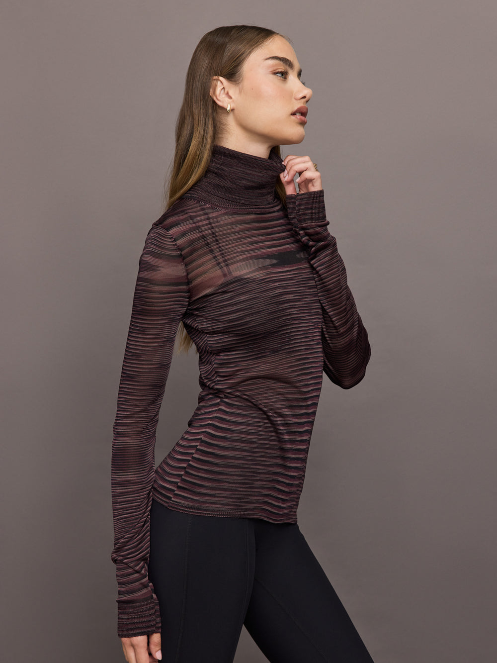 Model wears a striped sheer long sleeve turtleneck with brown and purple tones. 