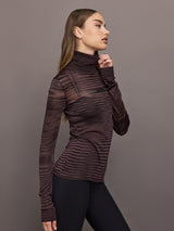 Model wears a striped sheer long sleeve turtleneck with brown and purple tones. 
