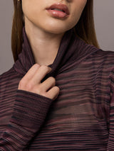Model wears a striped sheer long sleeve turtleneck with brown and purple tones. 