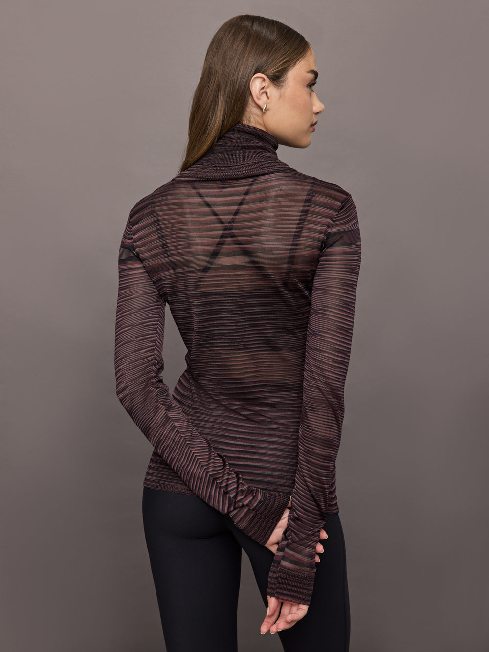 Model wears a striped sheer long sleeve turtleneck with brown and purple tones. 