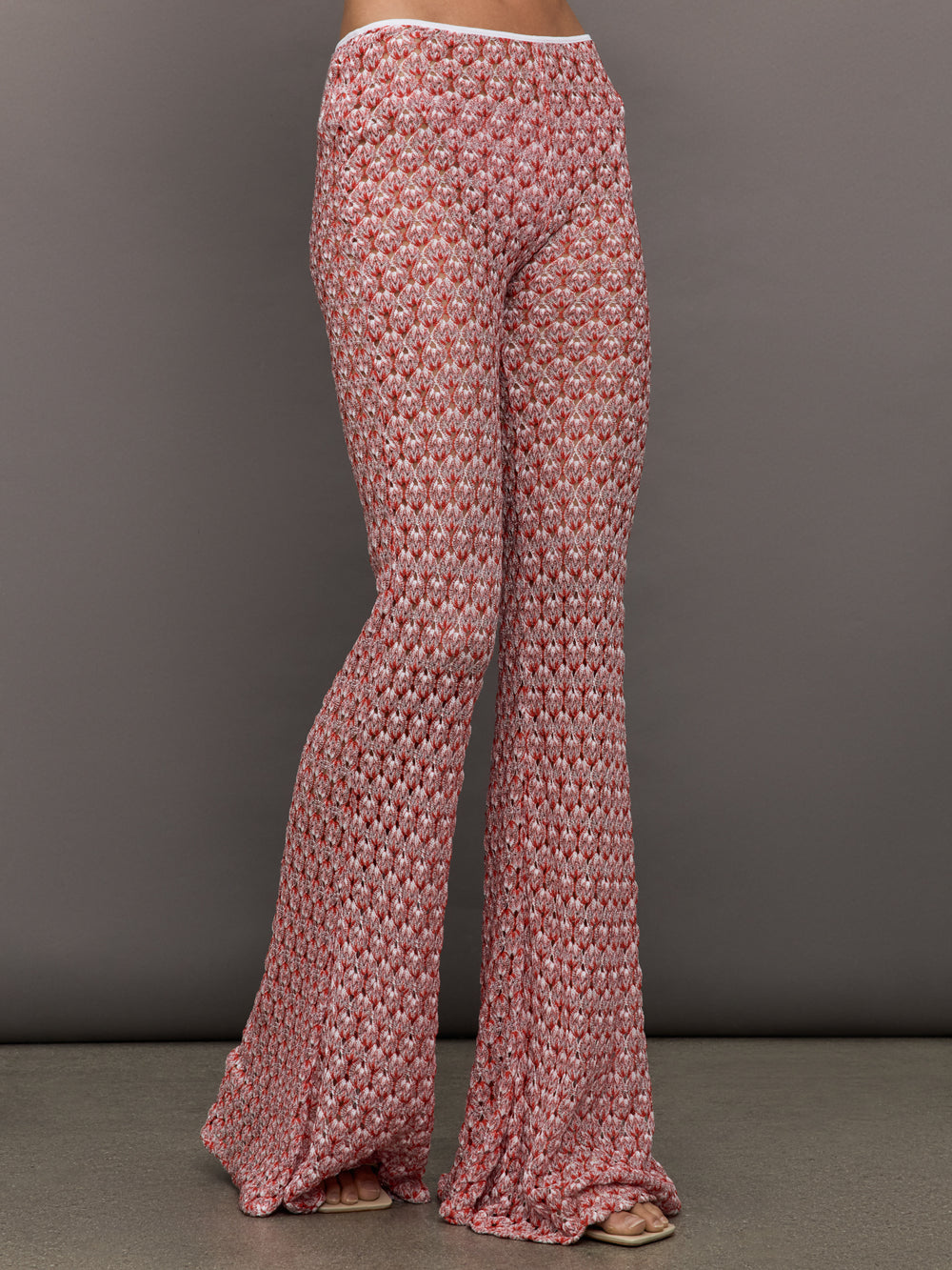 Model wears mid-waisted red flare trousers with an abstract patterned design throughout.