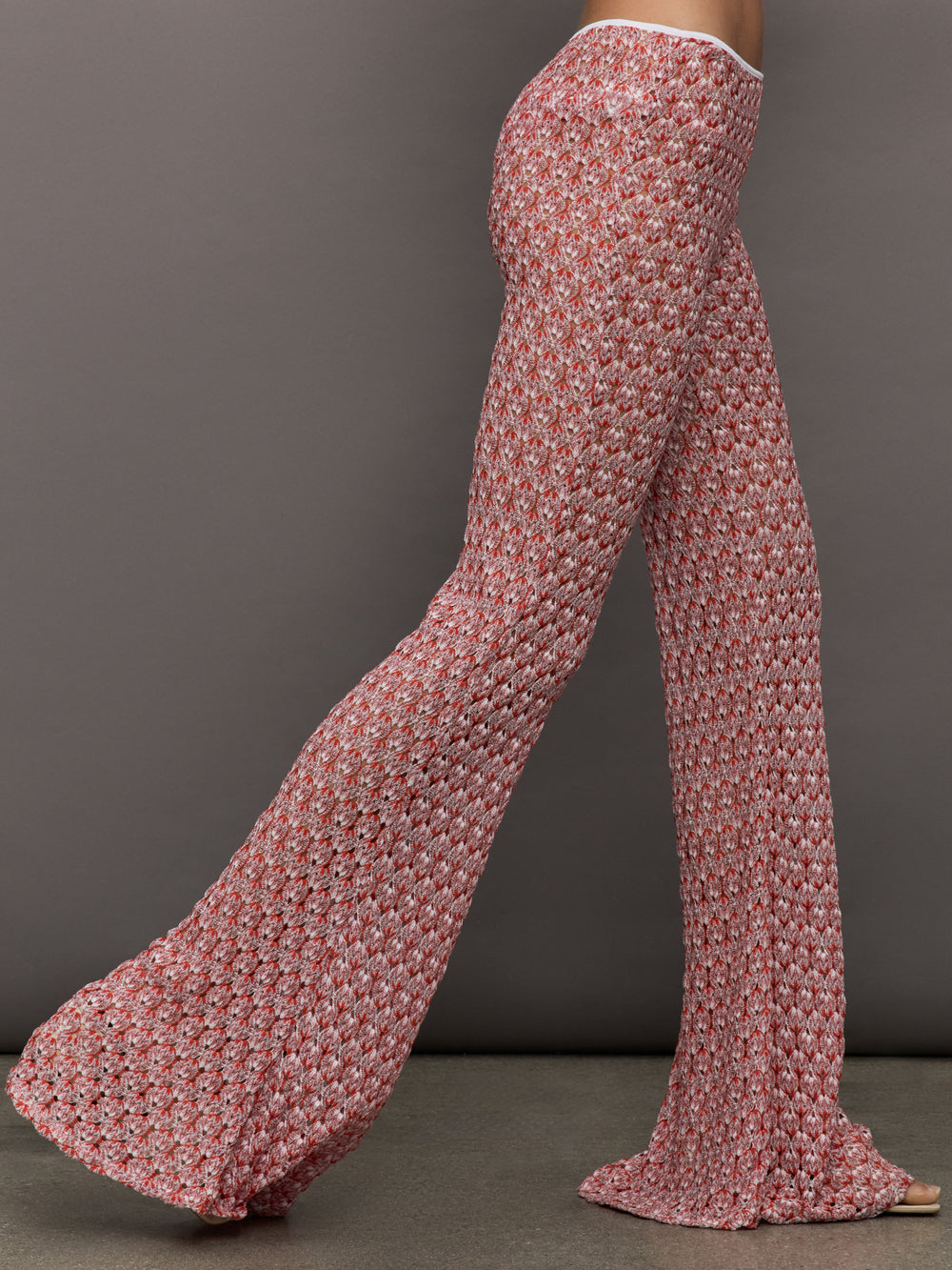 Model wears mid-waisted red flare trousers with an abstract patterned design throughout.