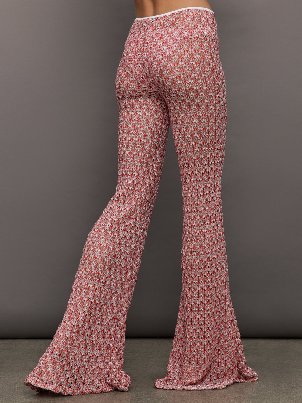 Model wears mid-waisted red flare trousers with an abstract patterned design throughout.