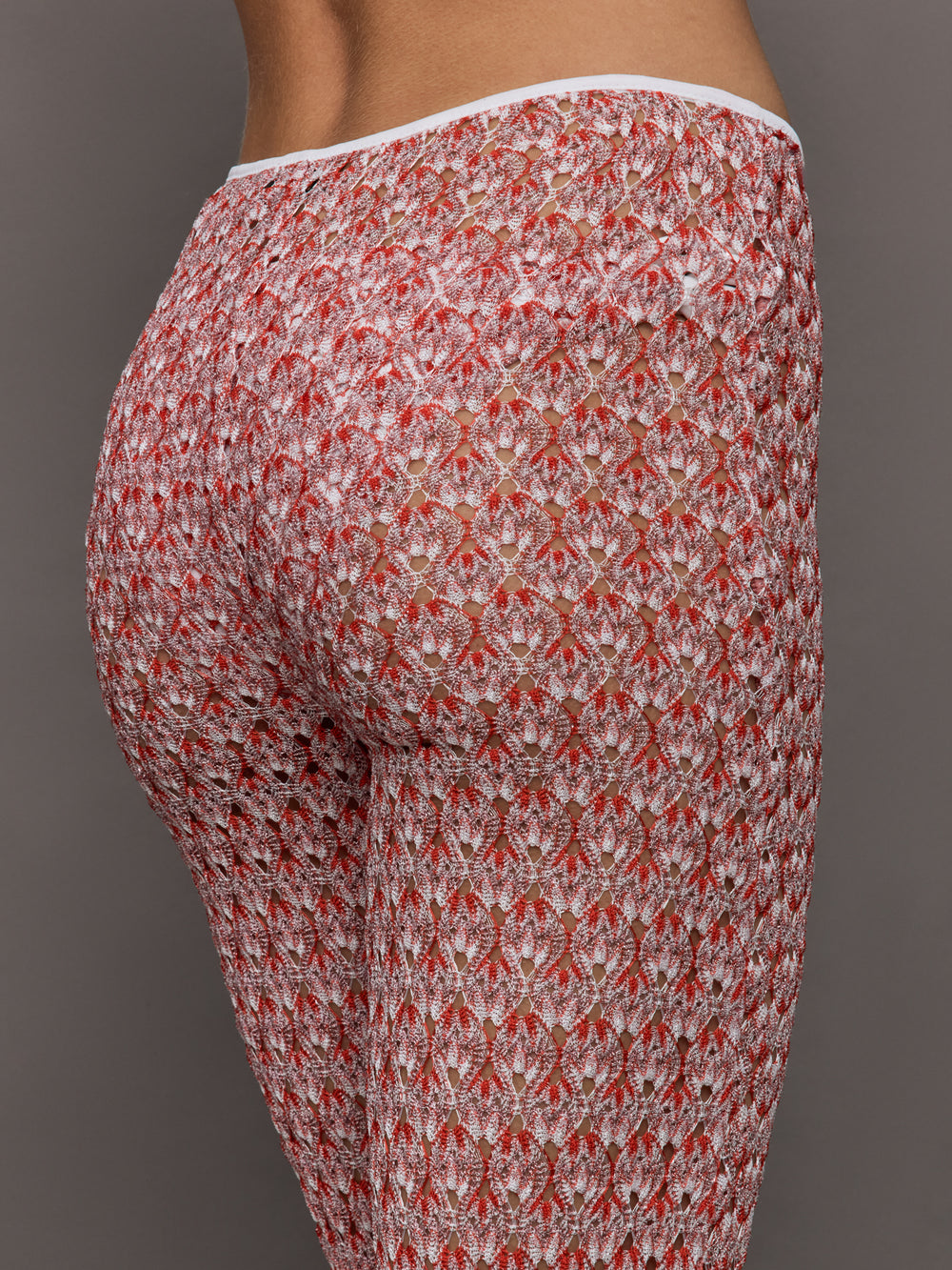 Model wears mid-waisted red flare trousers with an abstract patterned design throughout.