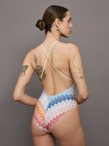 Model wears a one piece high cut bathing suit with a deep v neck and multicolored zig zag pattern. 