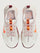 White running shoe with orange swoosh logo on a light gray background