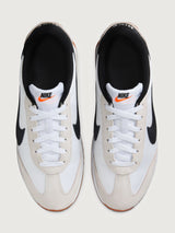 White and black sneaker with a brown sole on a light gray background