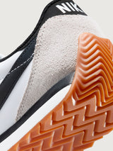 White and black sneaker with a brown sole on a light gray background