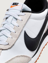 White and black sneaker with a brown sole on a light gray background