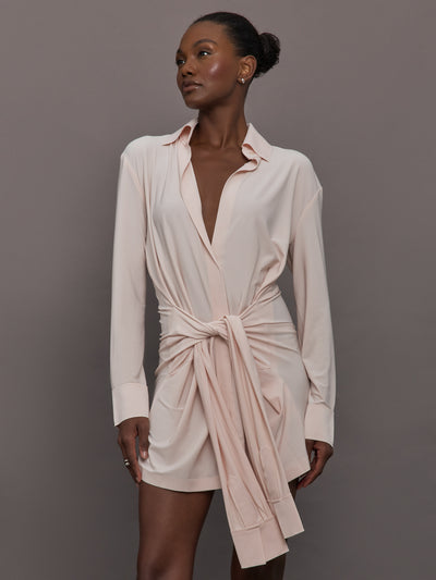 Model wears a baby pink Four Sleeve NK shirt mini dress featuring a collared neckline, button-down front, and layered four-sleeve detail with a structured, tailored fit