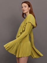Model wears long sleeve mini dress in asparagus green with a deep V-neckline and ruffle detailing.
