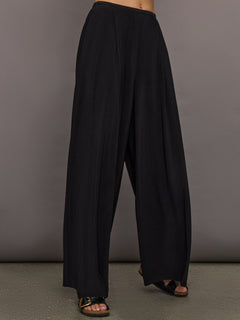 Model wears a pair of mid rise black pleated wide leg dress pants. 