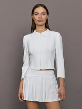 Model wears white jacket with a front zipper, collared neck and long sleeves.




