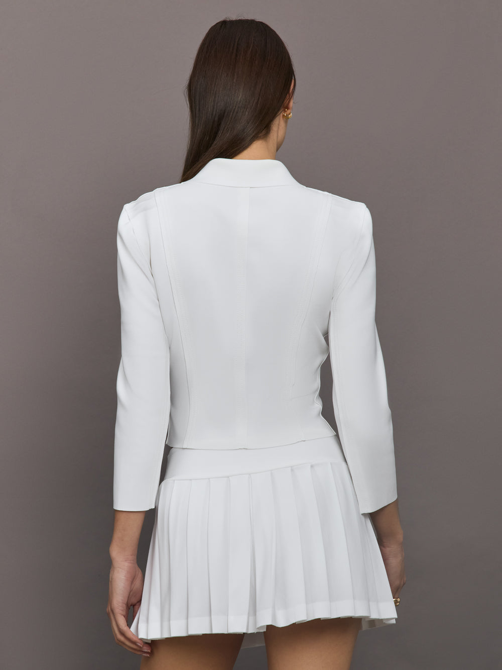 Model wears white jacket with a front zipper, collared neck and long sleeves.
