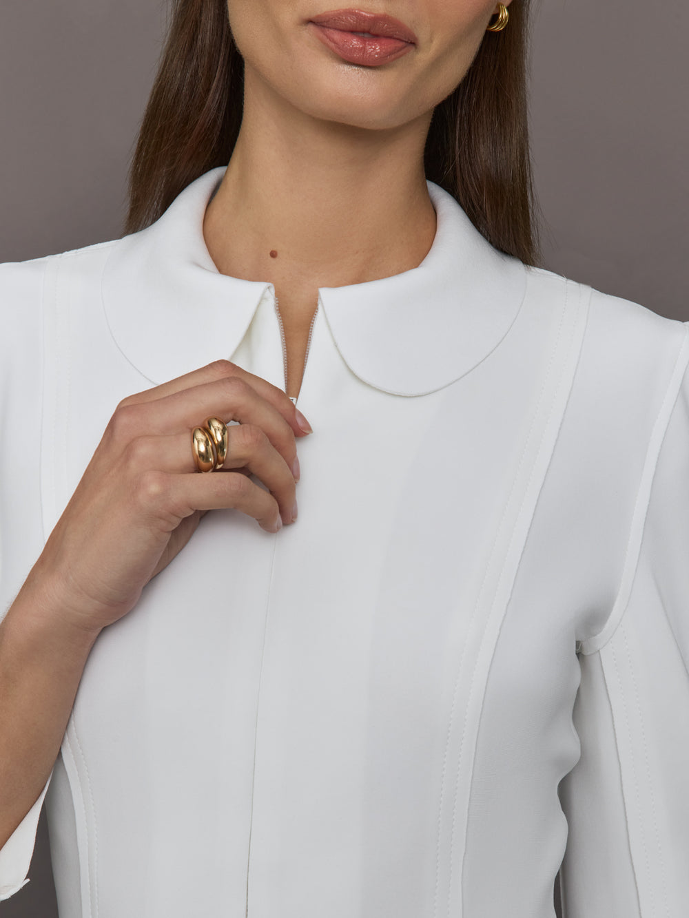 Model wears white jacket with a front zipper, collared neck and long sleeves.
