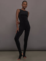 Model wears a black sleeveless X catsuit with built-in footies, featuring a high neckline, body-contouring fit, and crisscross X straps on the back