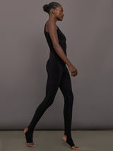Model wears a black sleeveless X catsuit with built-in footies, featuring a high neckline, body-contouring fit, and crisscross X straps on the back
