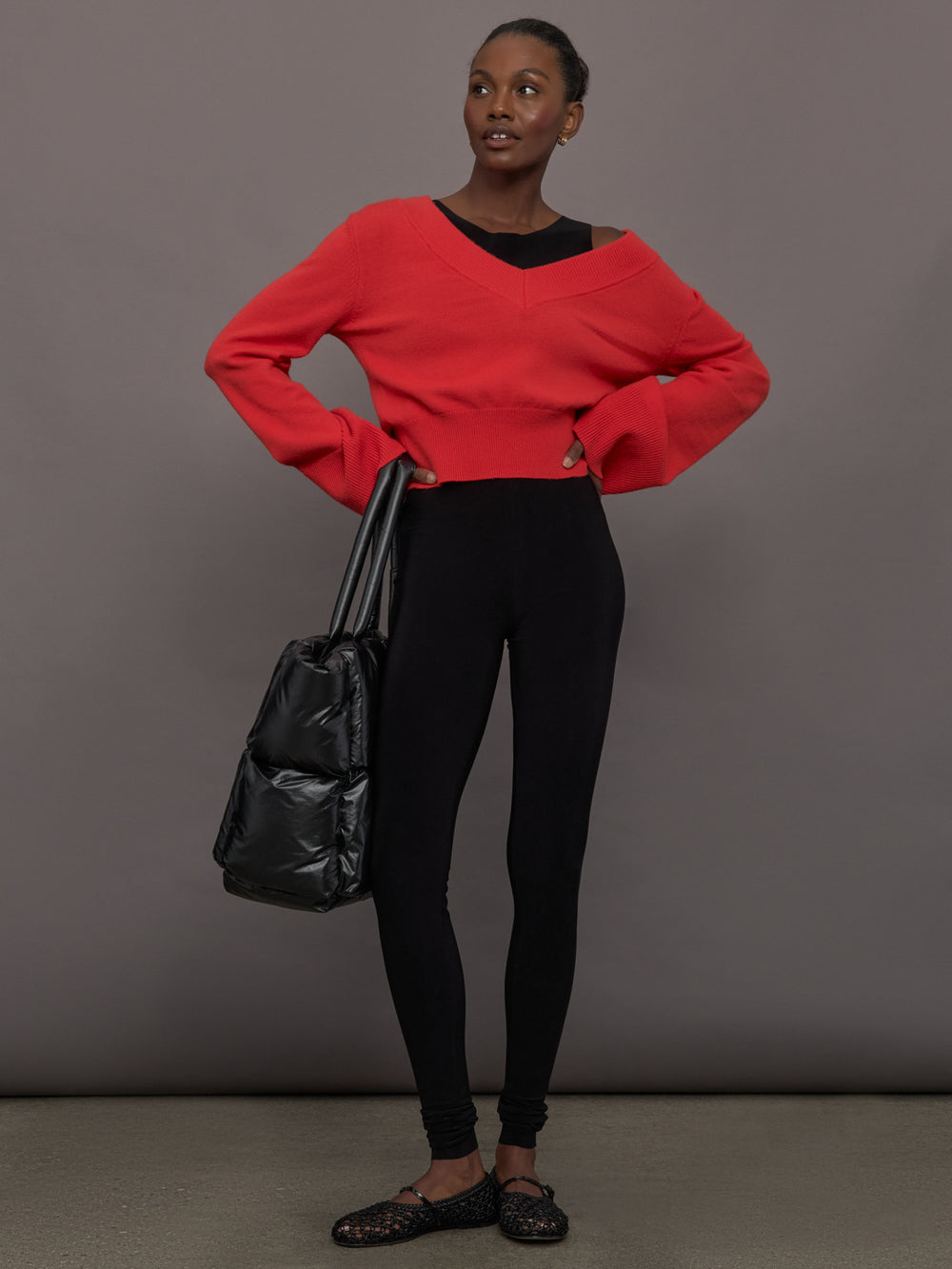 Model wears a black sleeveless X catsuit with built-in footies, featuring a high neckline, body-contouring fit, and crisscross X straps on the back