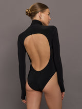 Person wearing a black bodysuit with an open back against a gray background
