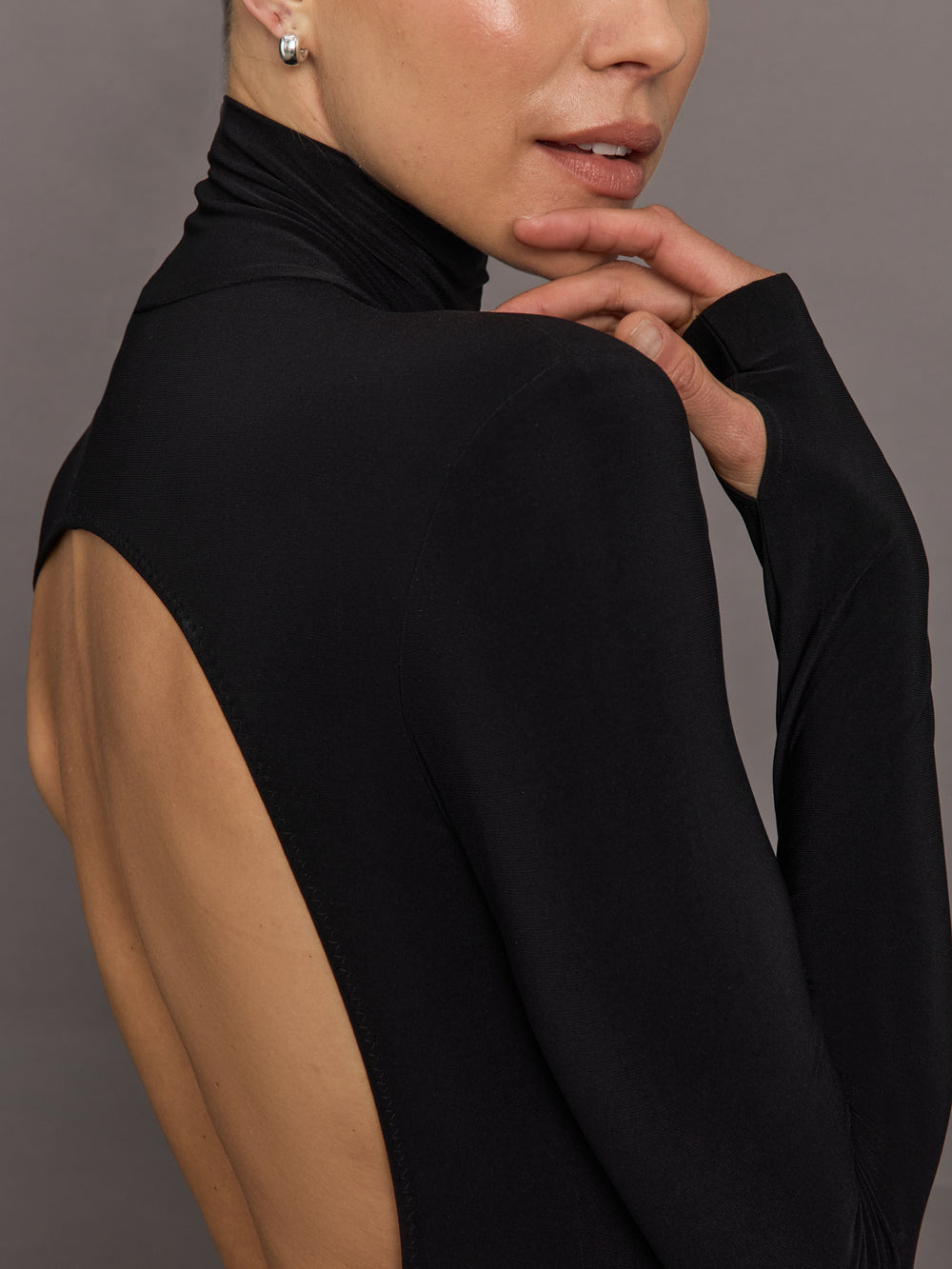 Person wearing a black turtleneck with an open back on a gray background