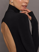 Person wearing a black turtleneck with an open back on a gray background