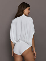 Woman wearing a white bodysuit against a brown background