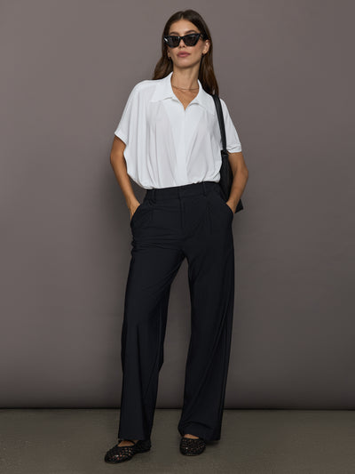 Woman wearing a white shirt and black pants against a gray background