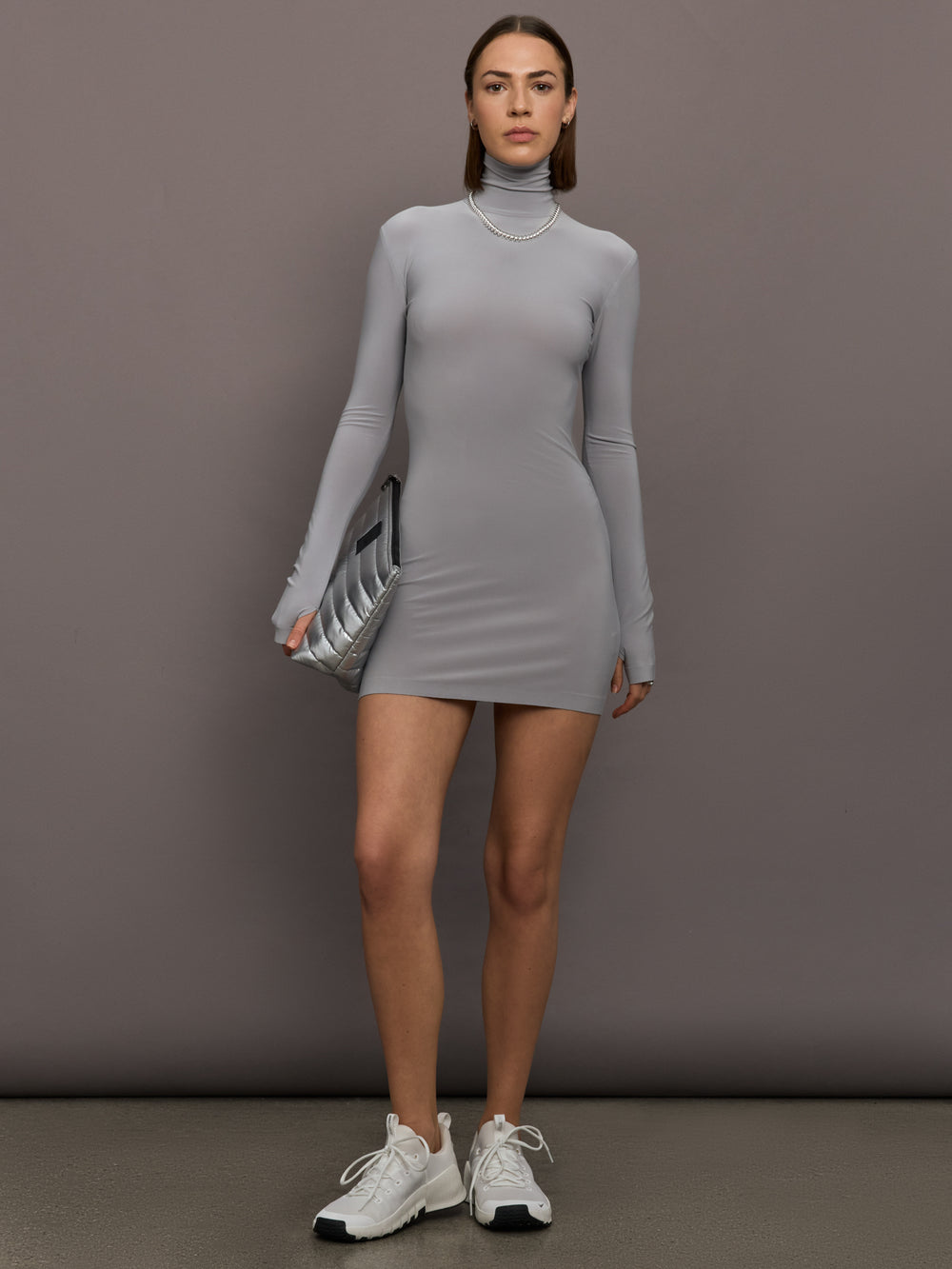 Model is wearing Long Sleeve Turtleneck Mini Dress in Grey, full body view styled with sneakers and clutch.
