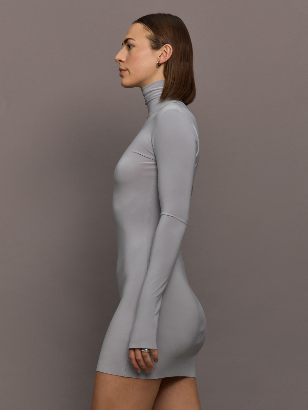 Model is wearing Long Sleeve Turtleneck Mini Dress in Grey, side view showing contoured silhouette and long sleeves.
