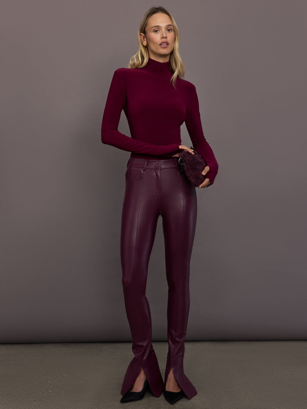Model is wearing Slim Fit Long Sleeve Turtle Top in Plum, full body front view styled with vegan leather pants.