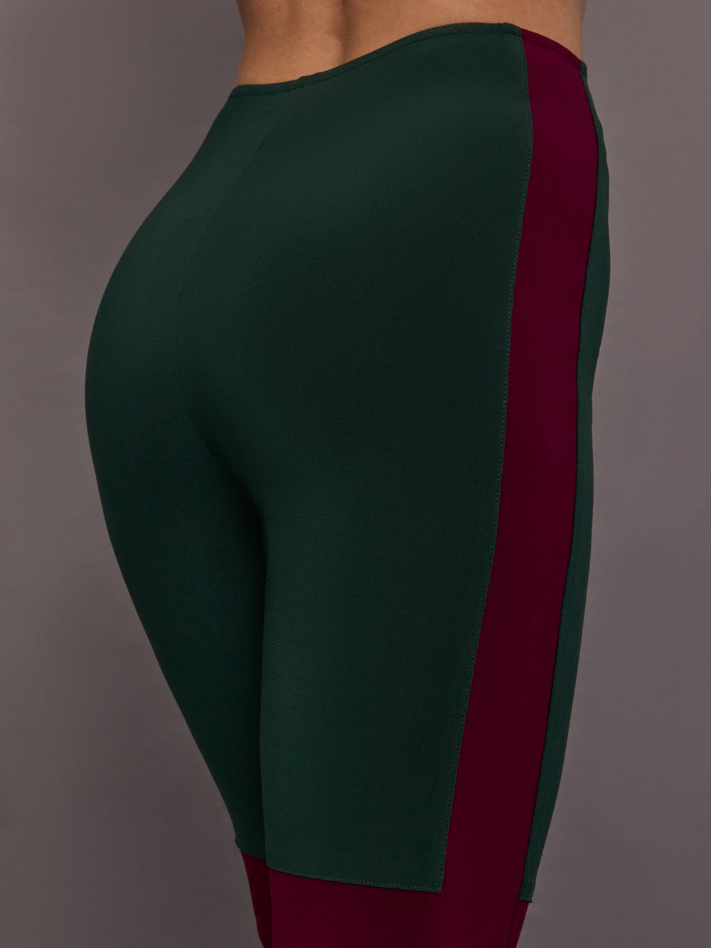 Model is wearing Side Stripe Legging With Knee Patch in Dark Emerald and Plum, close-up of side stripe and hip panel.