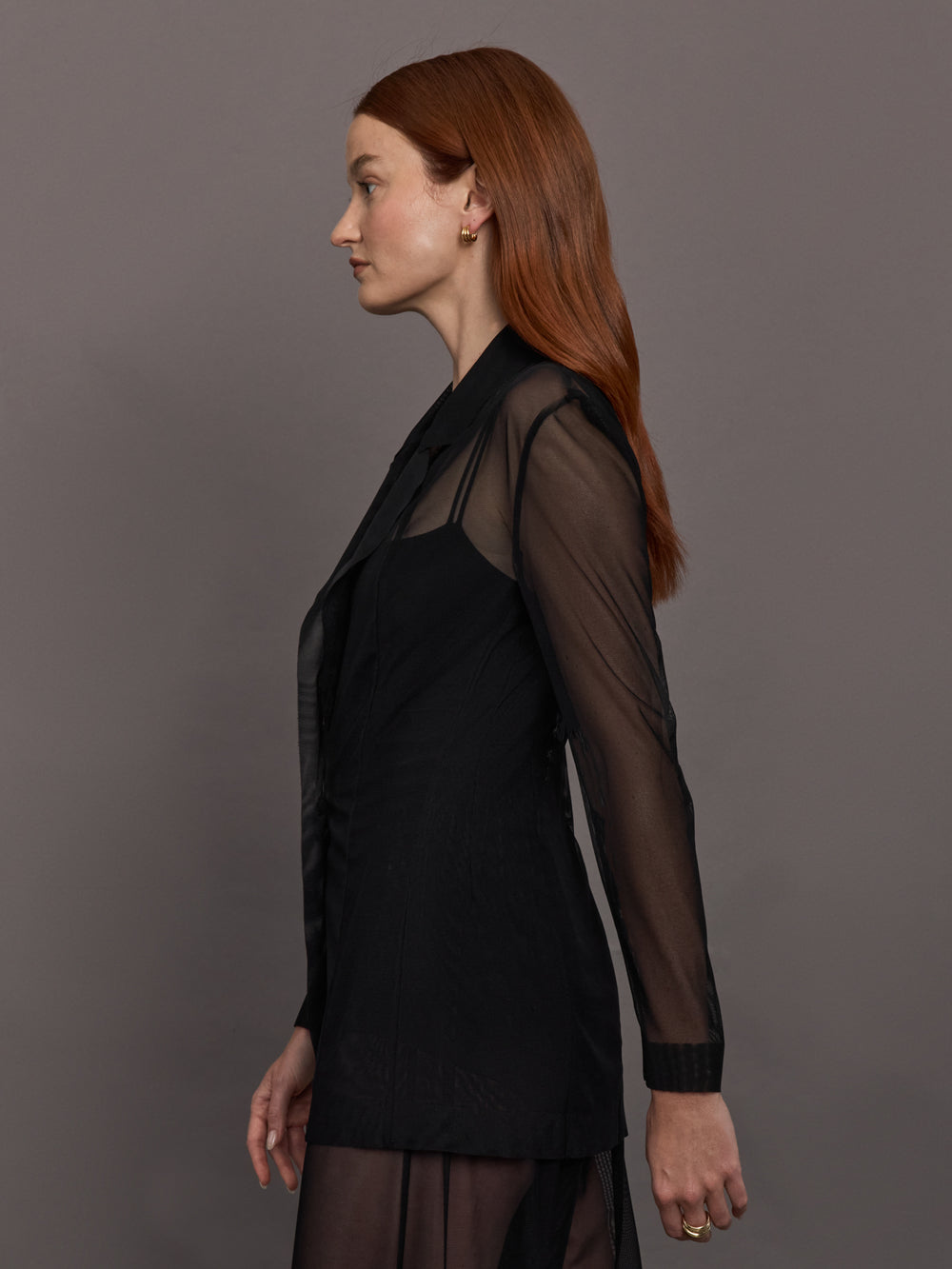 Model wears black single-breasted mesh jacket with a collared neck and tailored fit.
