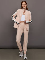 Model wears baby pink jacket with a turtleneck, front zipper, and side stripes on the sleeves.
