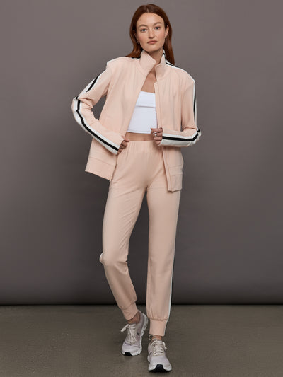 Model wears baby pink jacket with a turtleneck, front zipper, and side stripes on the sleeves.
